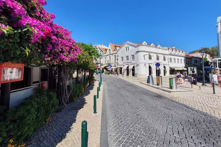 Charming cobblestone street in Cascais adorned with pink blossoms and traditional Portuguese architecture.