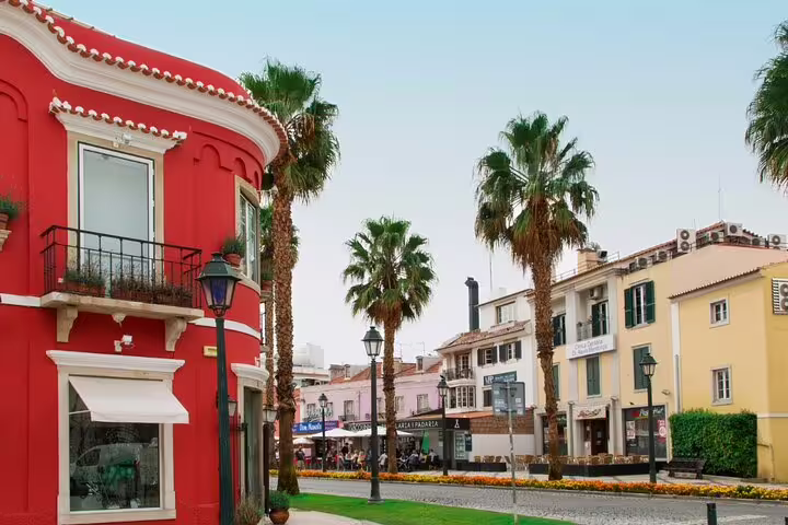 Vibrant street scene in Cascais with colorful buildings and palm trees, featured in a full-day tour of Sintra and surroundings.