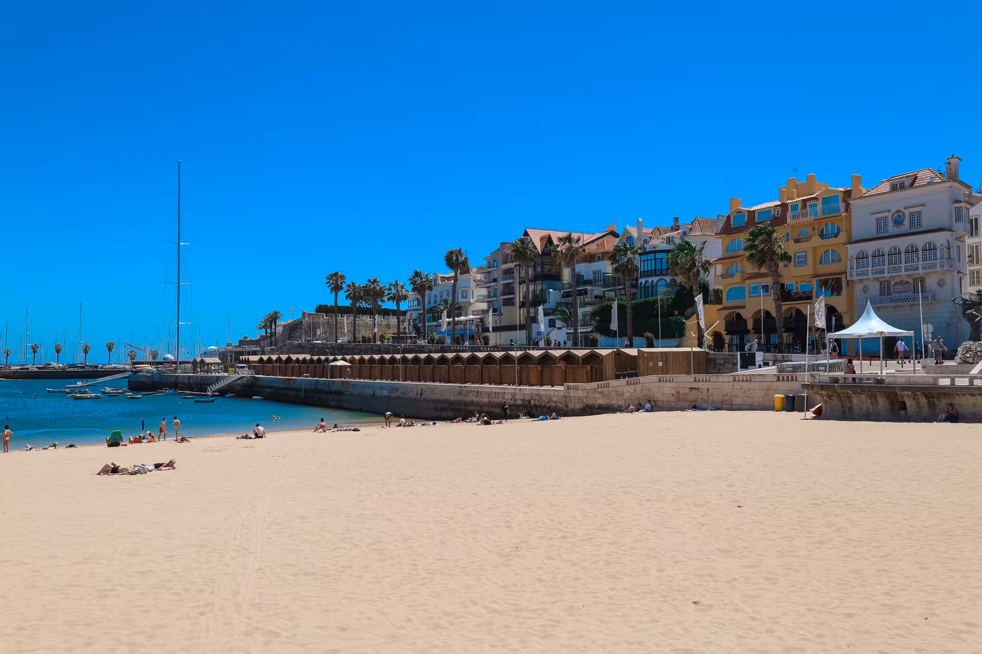 Sunny beach scene with colorful houses and boats in Cascais, a charming stop near Lisbon.