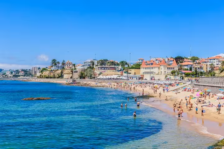 Sunbathers enjoy the golden sands and clear waters of Estoril Beach on a sunny day in Cascais, Portugal.