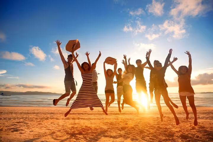 Group of friends jumping joyfully on Cascais Estoril Beach at sunset, highlighting a vibrant Lisbon tour experience.