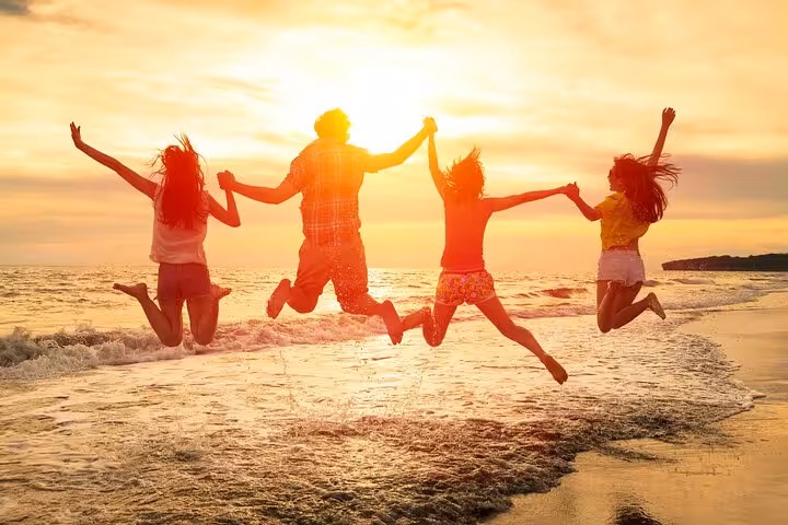 Group of friends joyfully jumping on Estoril Beach at sunset, capturing the essence of a vibrant beach getaway.