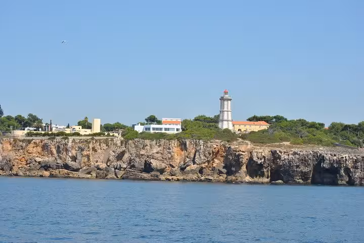 Santa Marta Lighthouse and rugged Cascais cliffs seen from a private sailing cruise, Atlantic coast Portugal with drinks