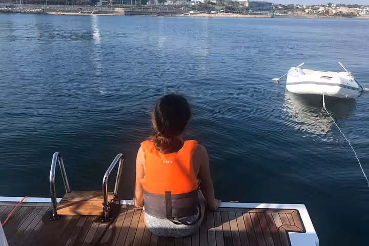 Guest relaxing on yacht swim platform in Cascais bay during private 2-hour sailing cruise with drinks