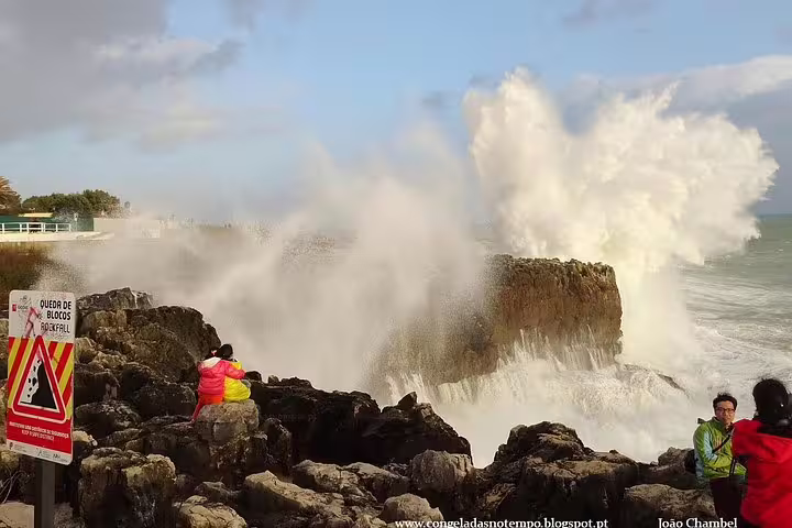 Visitors admire powerful ocean waves crashing against rocky cliffs in Cascais during a Sintra and Pena Palace day tour.