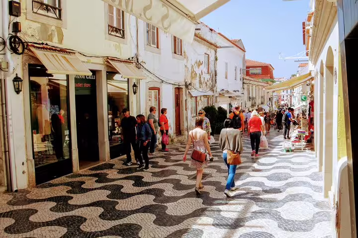 Tourists explore a charming pedestrian street in Cascais Village, featuring unique cobblestone patterns and vibrant shops.