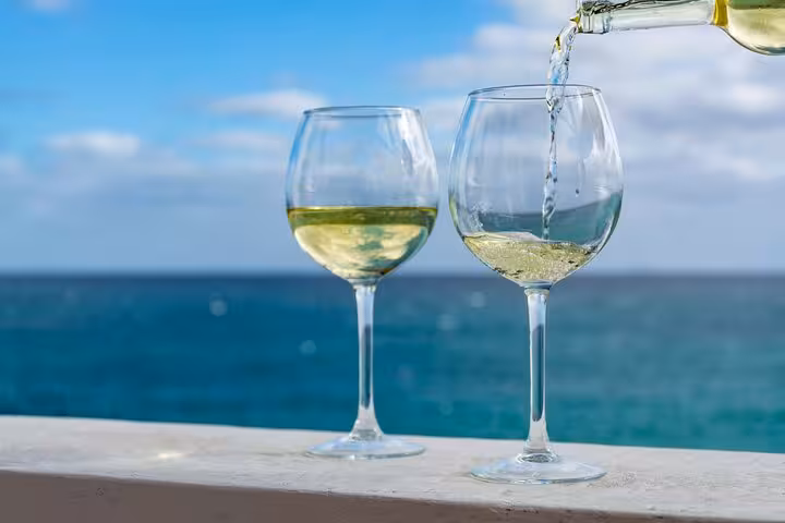Pouring white wine into glasses with a stunning ocean backdrop, ideal for a wine tasting experience near Cascais.