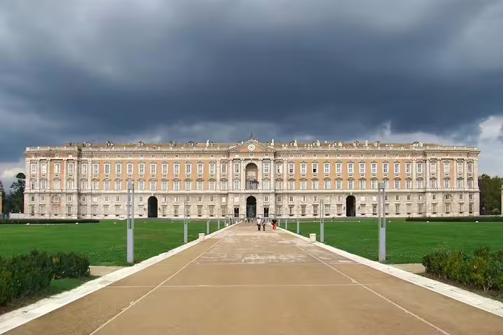 Grand façade of the Royal Palace of Caserta with visitors walking up the central avenue on a small-group guided tour