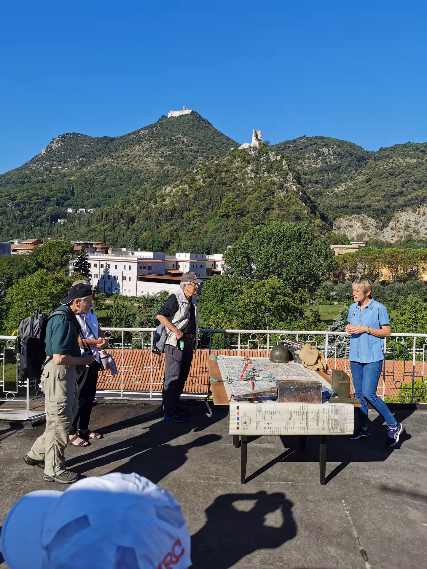 Group exploring Cassino's historical sites with a tour guide, set against a backdrop of green hills and clear skies.