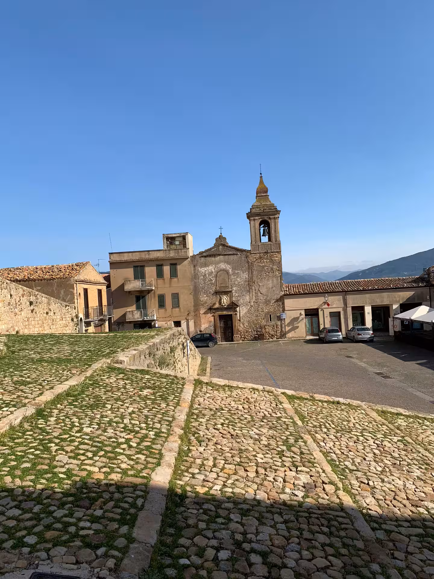 Historic stone church and bell tower overlooking cobbled streets in Castelbuono on a sunny private tour from Palermo