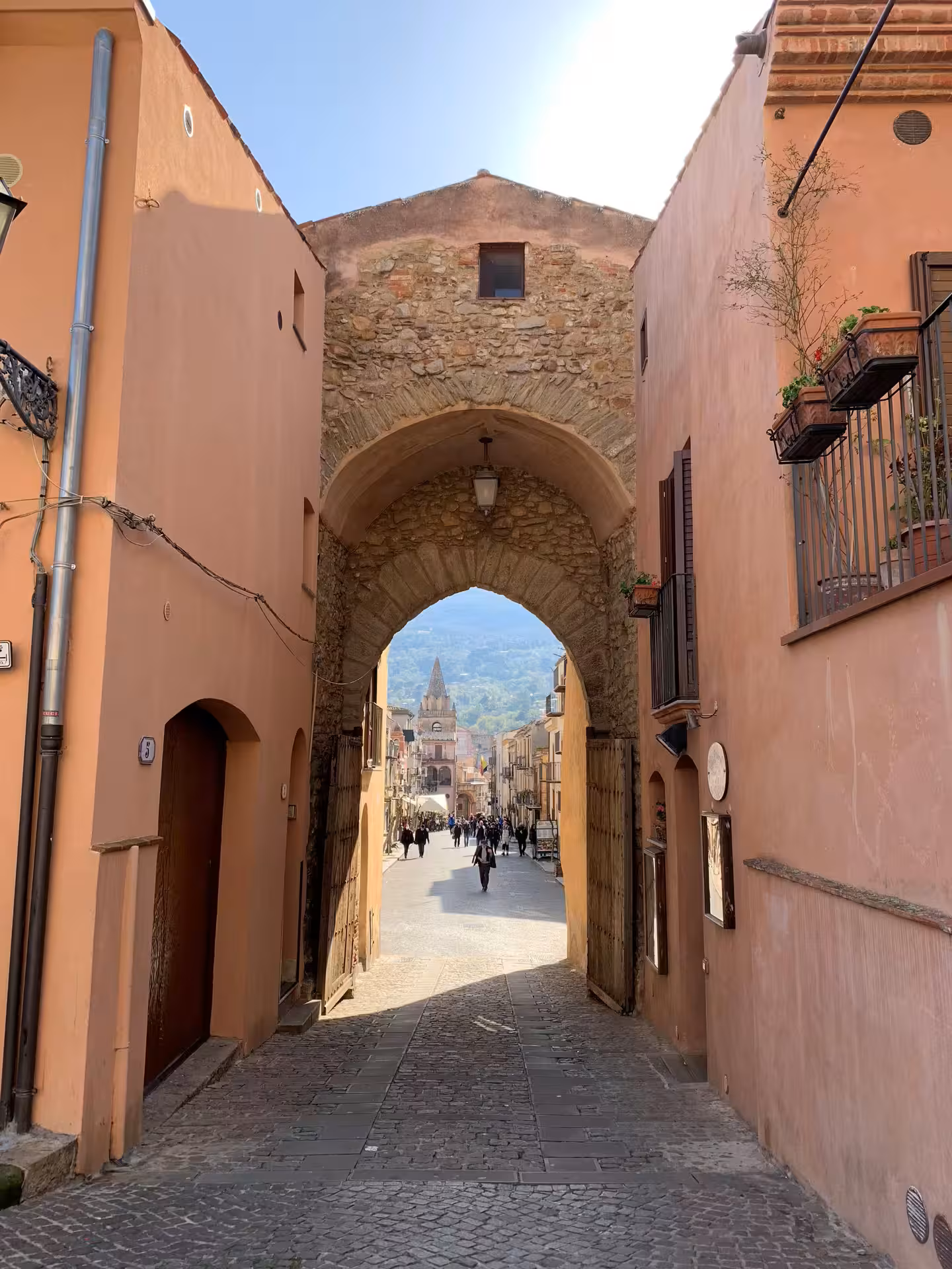 Medieval gate leading into Castelbuono old town with cobbled street, arches and mountain backdrop on Palermo tour