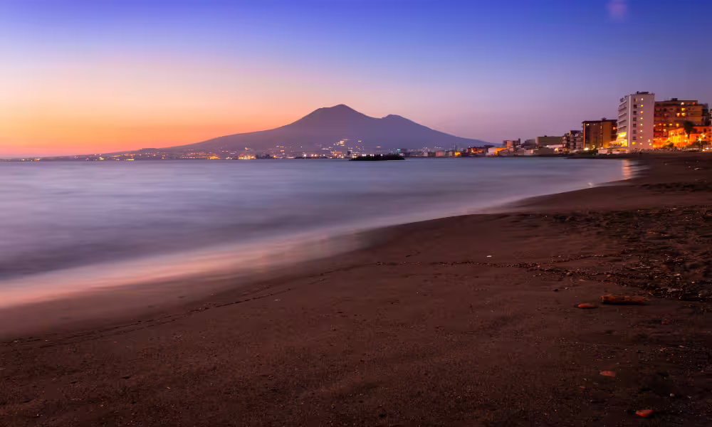 Sunset view of Castellammare beach with calm sea, city lights and Mount Vesuvius on the horizon during an overnight coastal stay