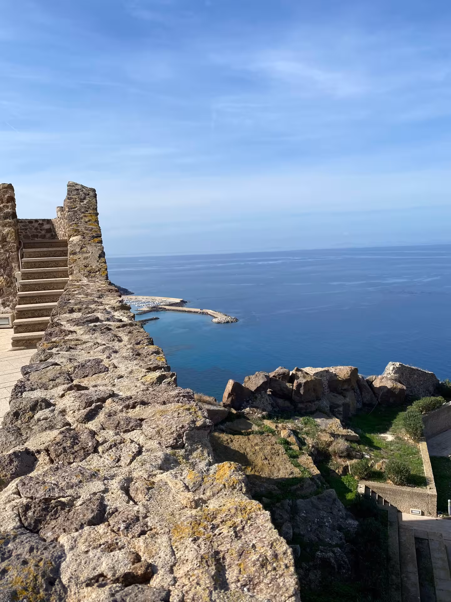 Scenic view of Castelsardo's ancient stone walls overlooking the vibrant blue Mediterranean Sea.