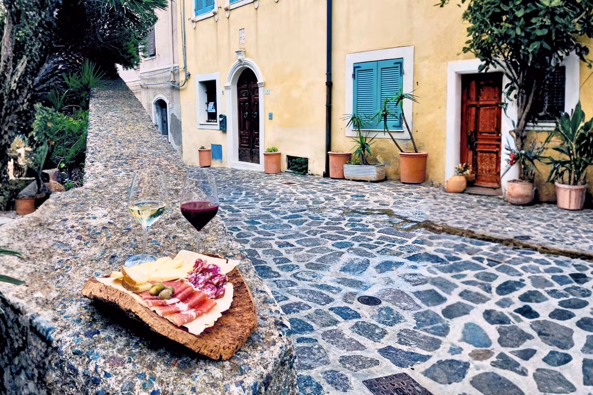 Charming Castelsardo cobblestone street with aperitif platter of meats and cheese alongside red and white wine.