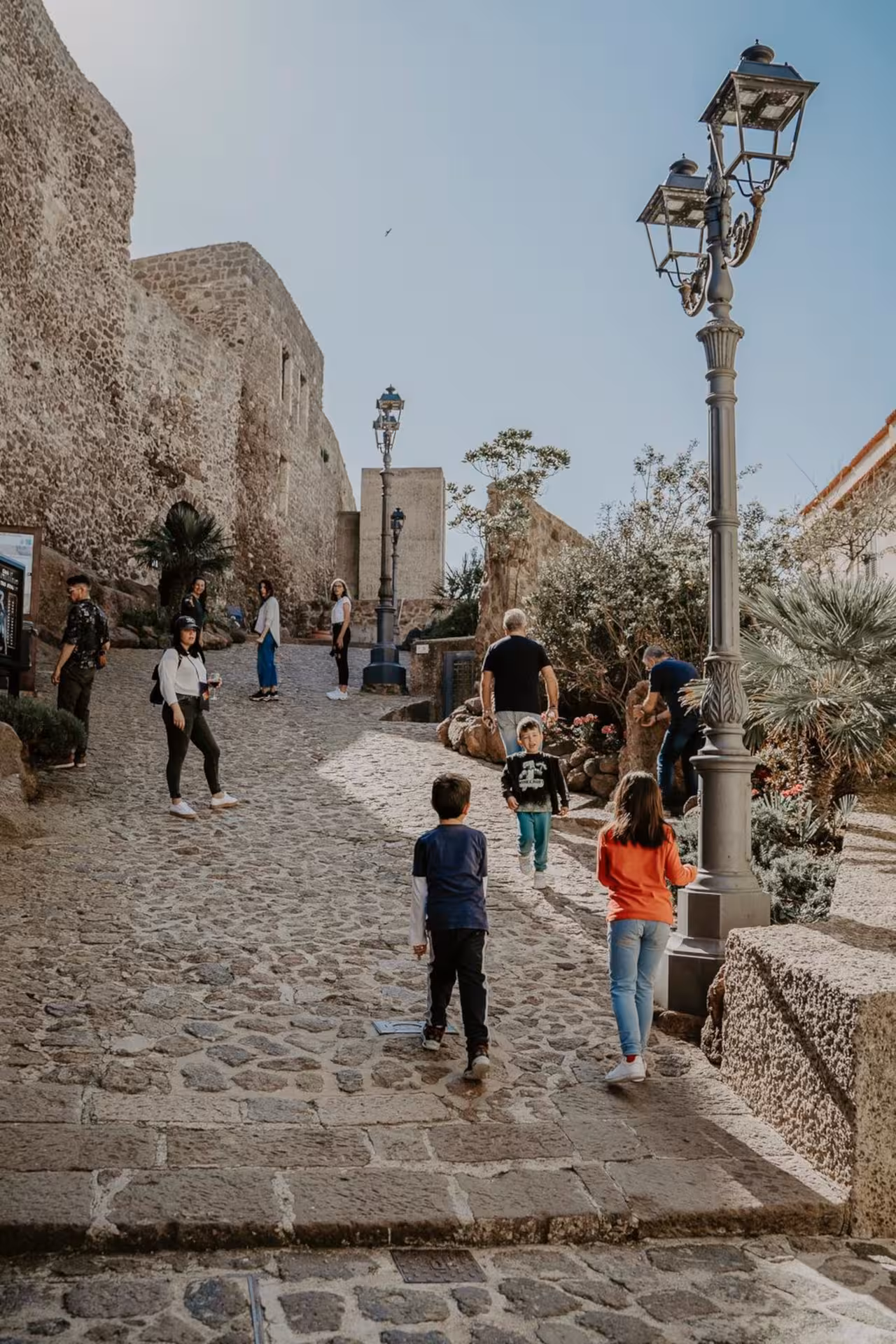 Visitors explore the historic cobblestone streets of Castelsardo under a clear blue sky.