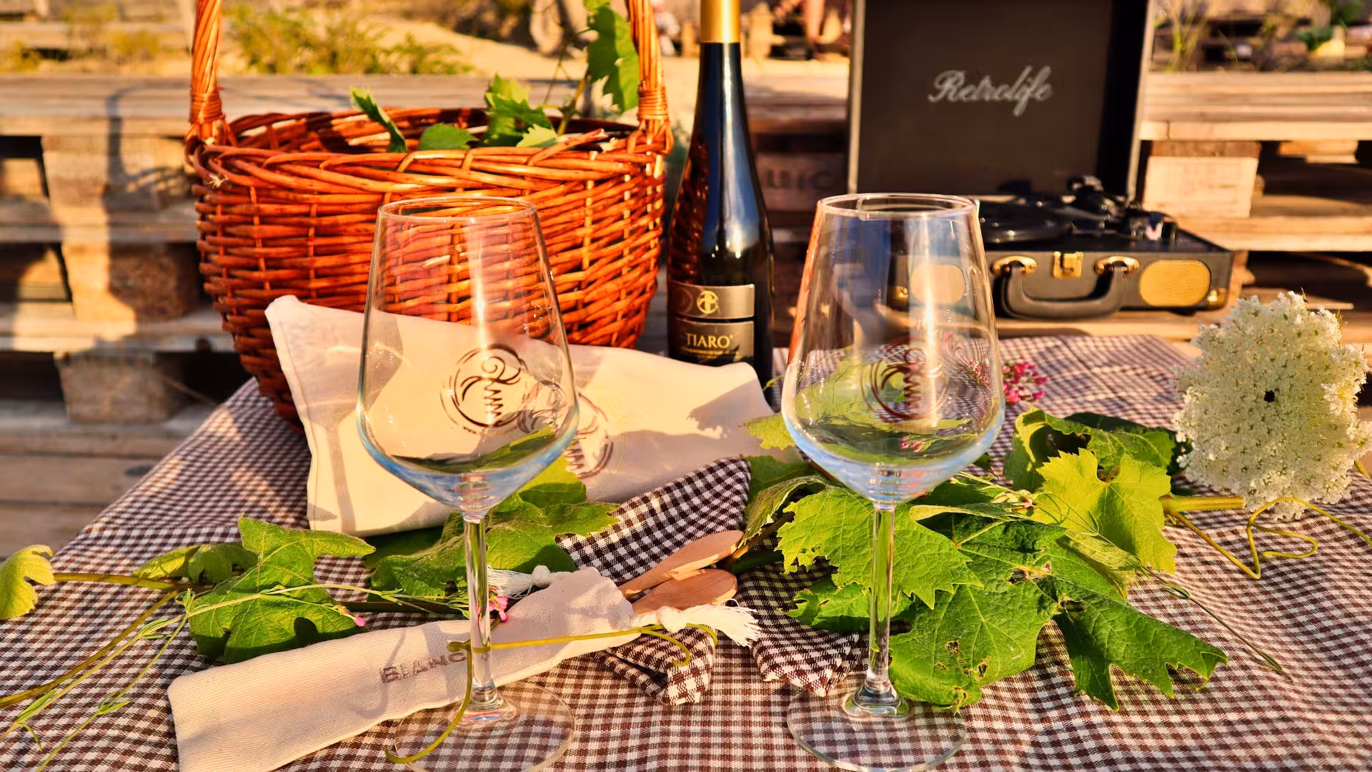 Elegant picnic setup with wine glasses, wicker basket, and bottle on a checkered cloth in Castelsardo estate.