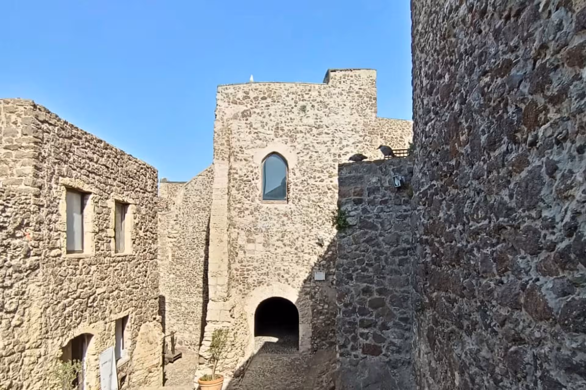 View of historic stone walls and archway in Castelsardo old town, highlighting medieval architecture under a bright sky.