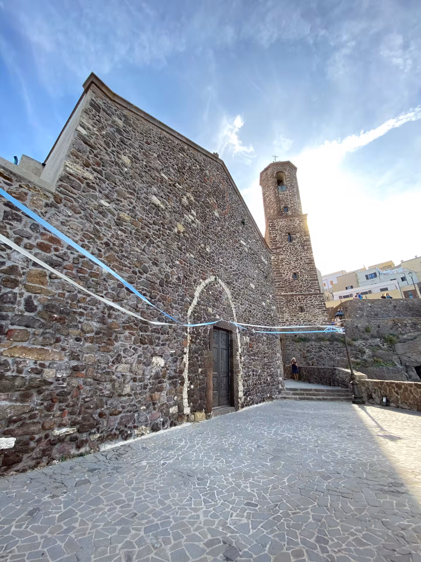 Historic stone building with a tower in Castelsardo, showcasing medieval architecture under a clear blue sky.