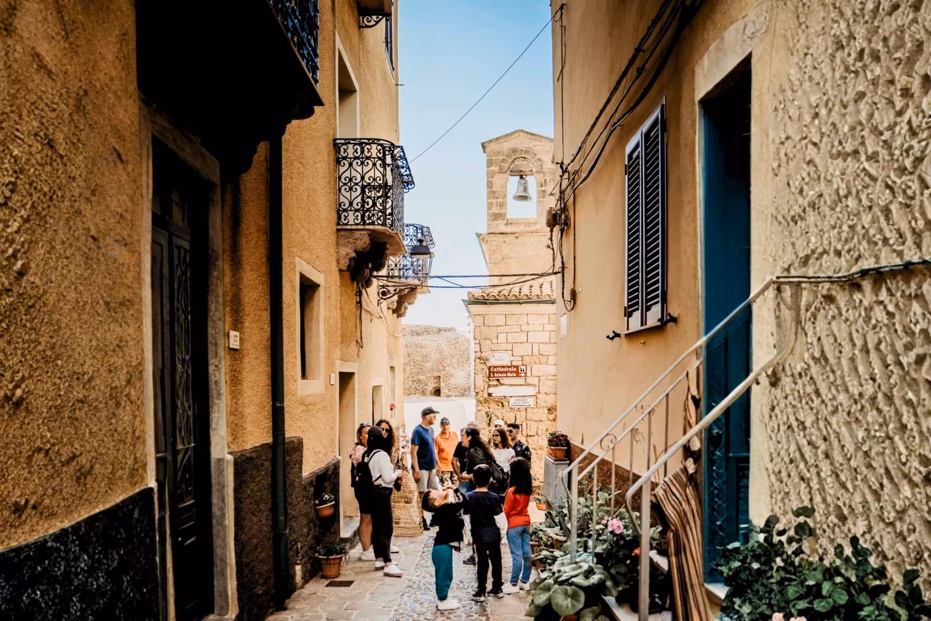 Tourists explore a charming narrow street in Castelsardo's historic old town, surrounded by rustic buildings.