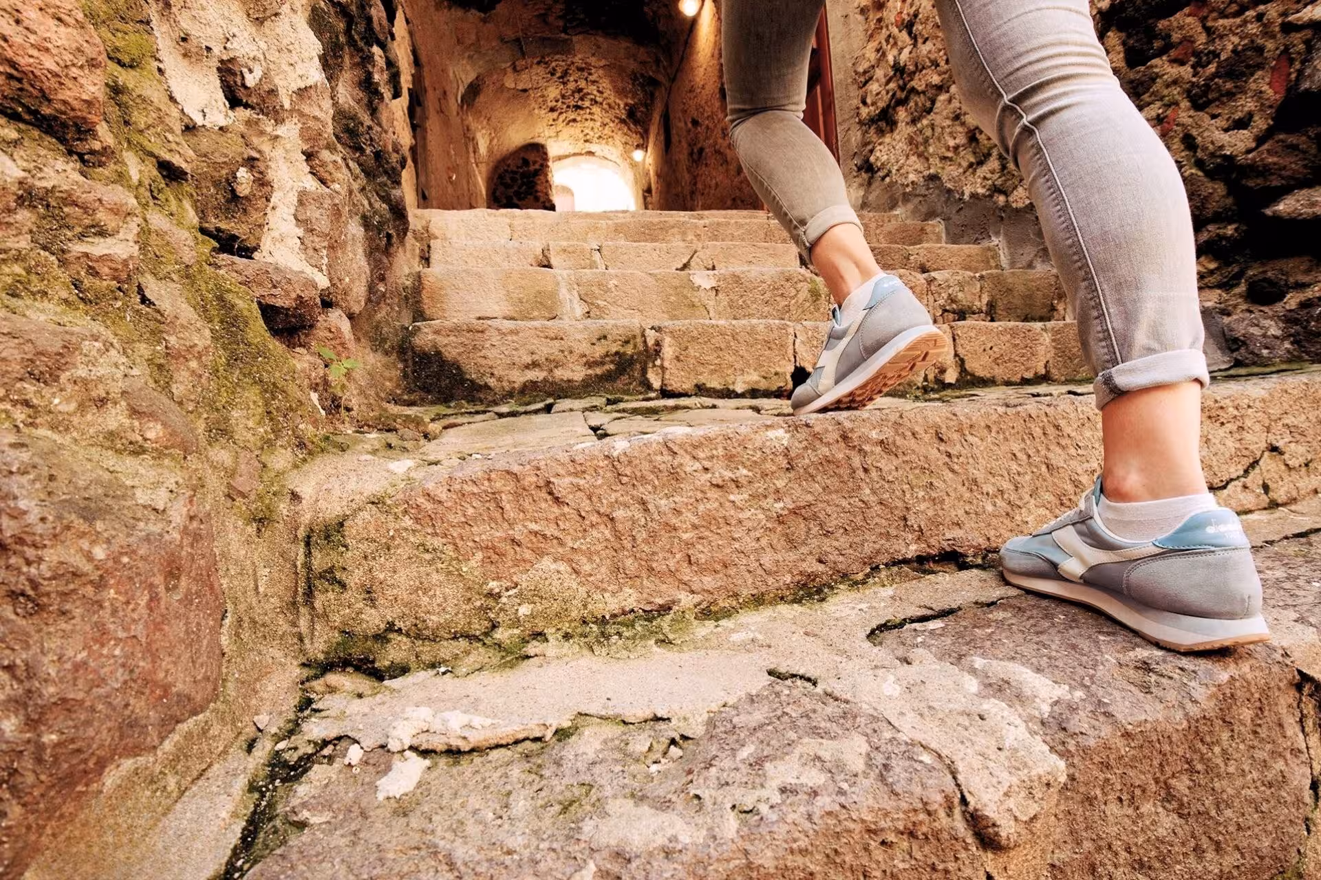 Traveler ascending ancient stone steps in Castelsardo's old town, surrounded by rustic stone walls.