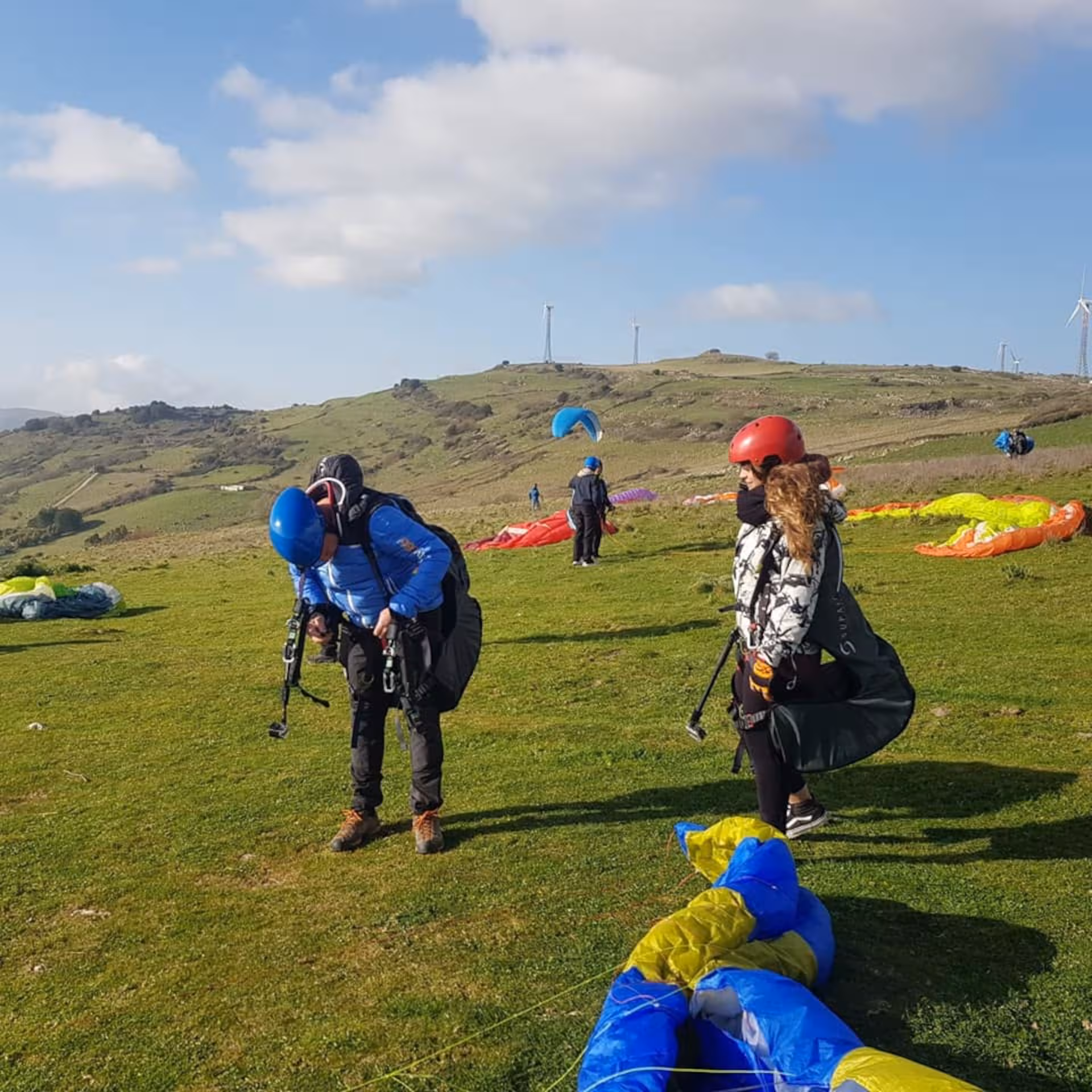 Paragliders preparing for tandem flight in Littigheddu with colorful canopies and scenic hills in the background.