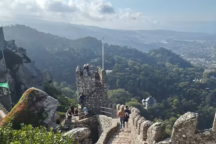 Panoramic view from the Castle of the Moors in Sintra, showcasing lush greenery and distant hills under a blue sky.