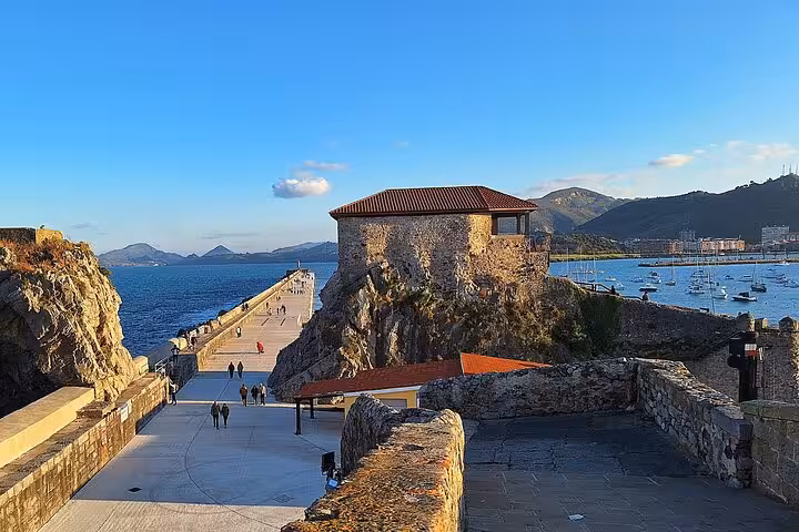 Scenic coastal view of Castro Urdiales with a historic stone building and a pier extending into the Bay of Biscay.