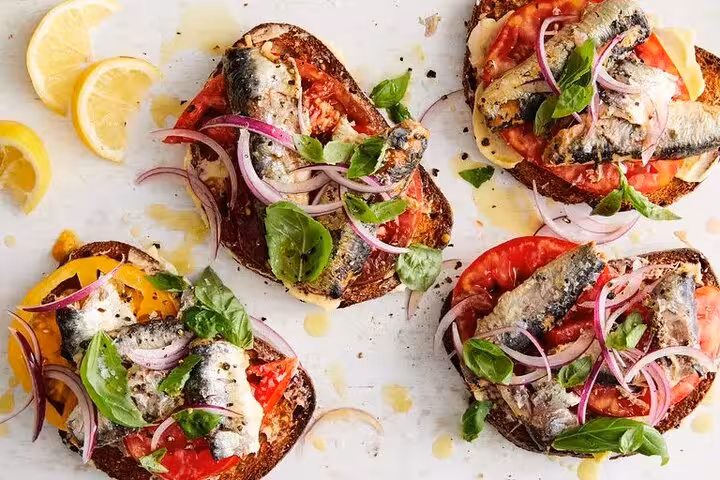 Delicious Catalan toasts topped with fresh sardines, tomatoes, basil, and red onions, perfect for a Gràcia food tour.