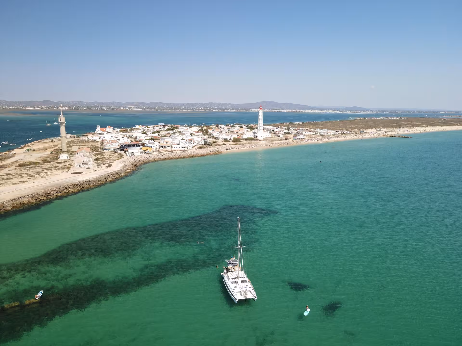 Catamaran anchored in the Blue Lagoon near Faro Island lighthouse, Algarve, on a half-day sailing tour