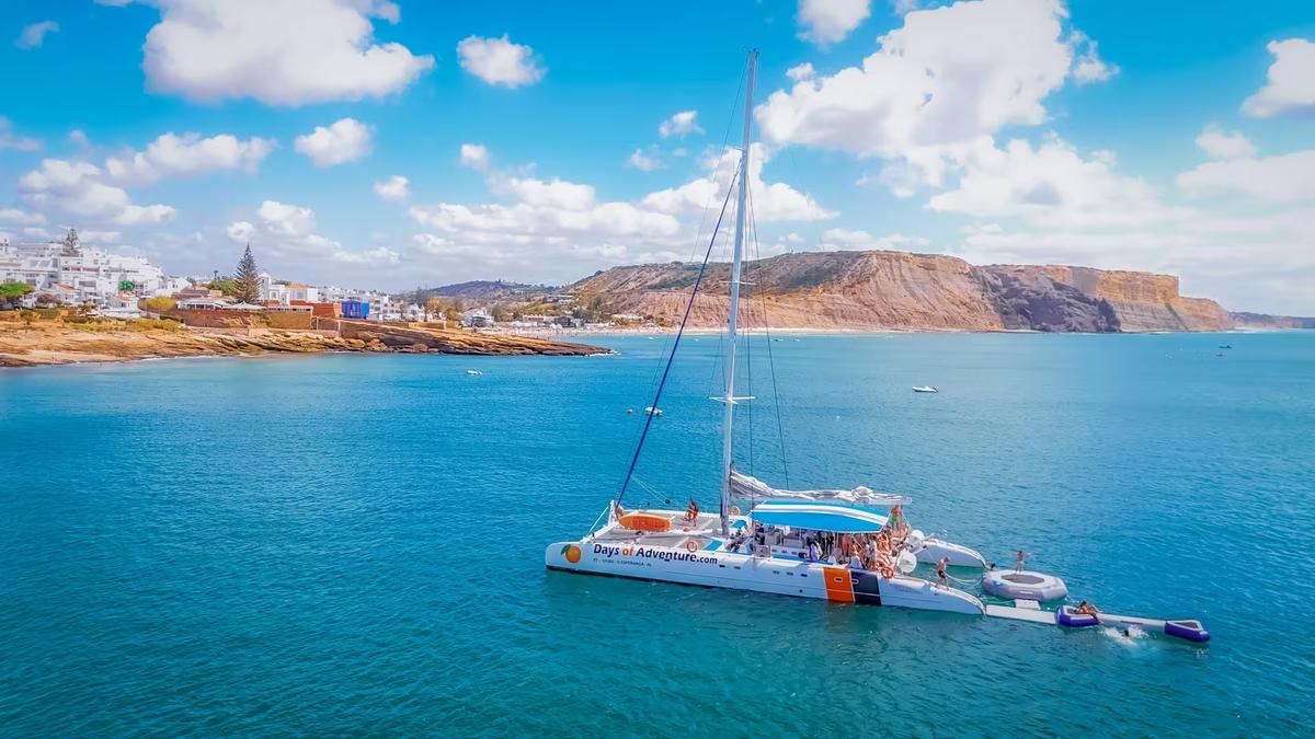 Aerial view of a catamaran anchored in turquoise Lagos waters with guests enjoying music and drinks on deck.