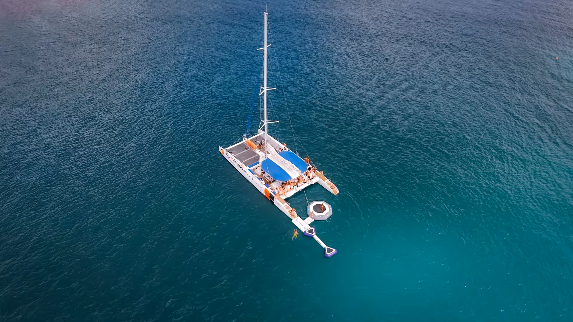 Aerial view of catamaran anchored in turquoise Lagos waters with floating trampoline and swimmers