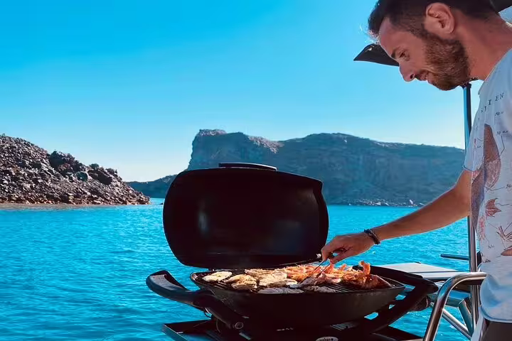 Man grilling seafood on a catamaran with stunning Santorini cliffs in the background during a private cruise.