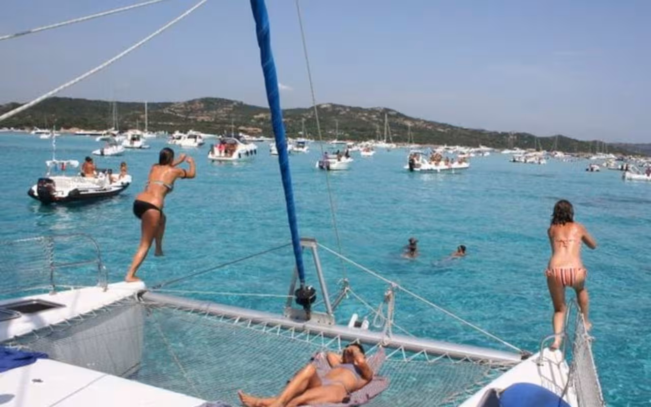 Visitors diving from a catamaran into the clear blue sea during a La Maddalena Archipelago island tour.