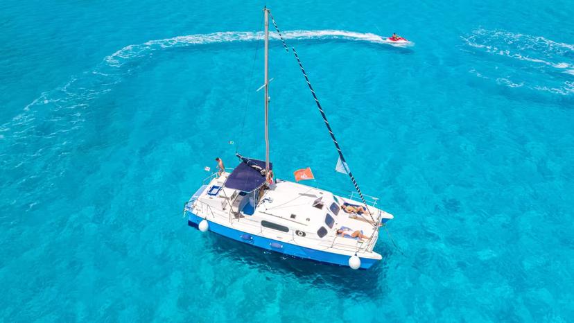 Aerial view of a catamaran sailing in the vibrant blue waters of the Gulf of Asinara, with a jet ski in the background.