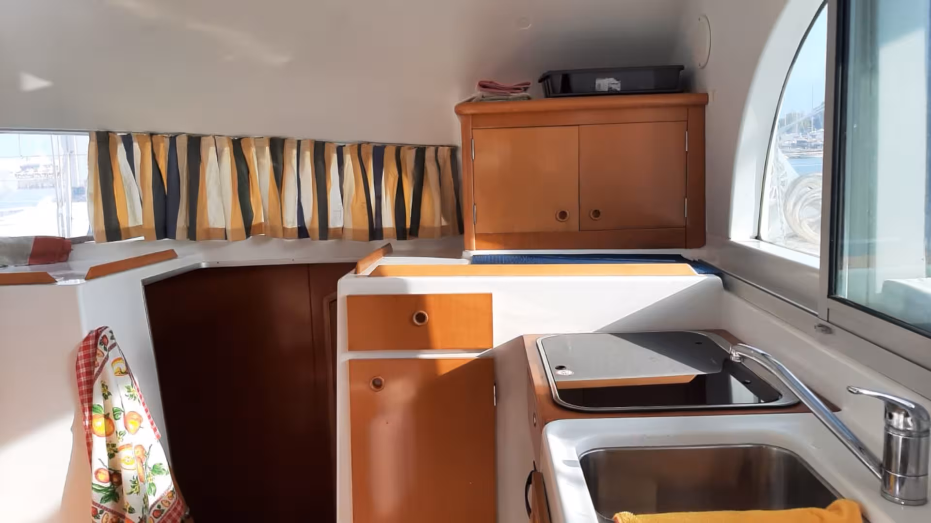 Modern kitchen area in catamaran Tenerè with ample storage and a view of La Maddalena Archipelago's coastline.