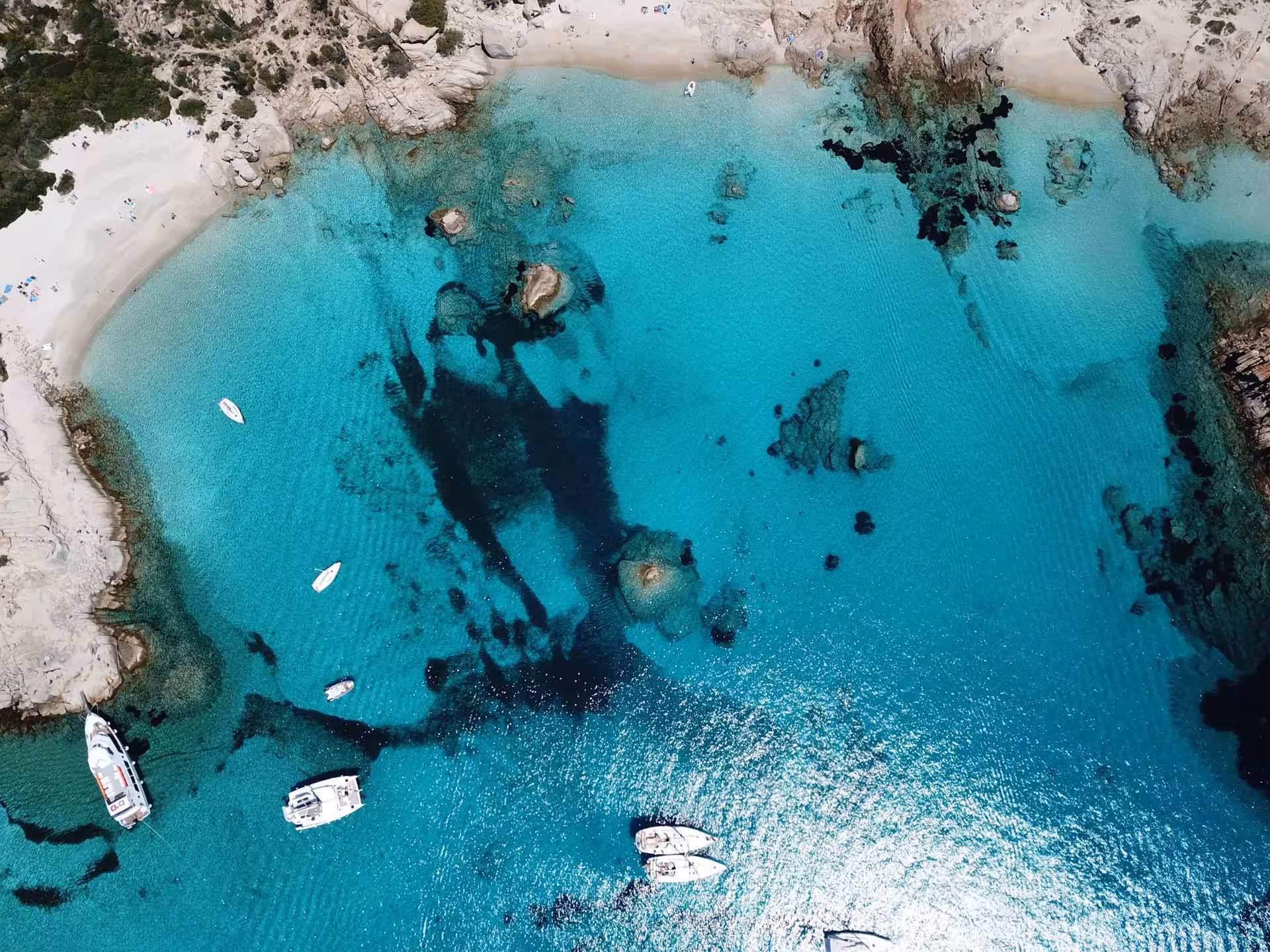 Aerial view of turquoise waters and boats in a bay of the La Maddalena Archipelago.
