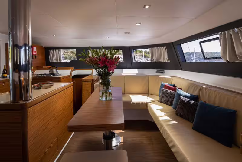 Spacious catamaran lounge with cushioned seating, flowers and panoramic windows for a relaxed Gulf of Naples day cruise