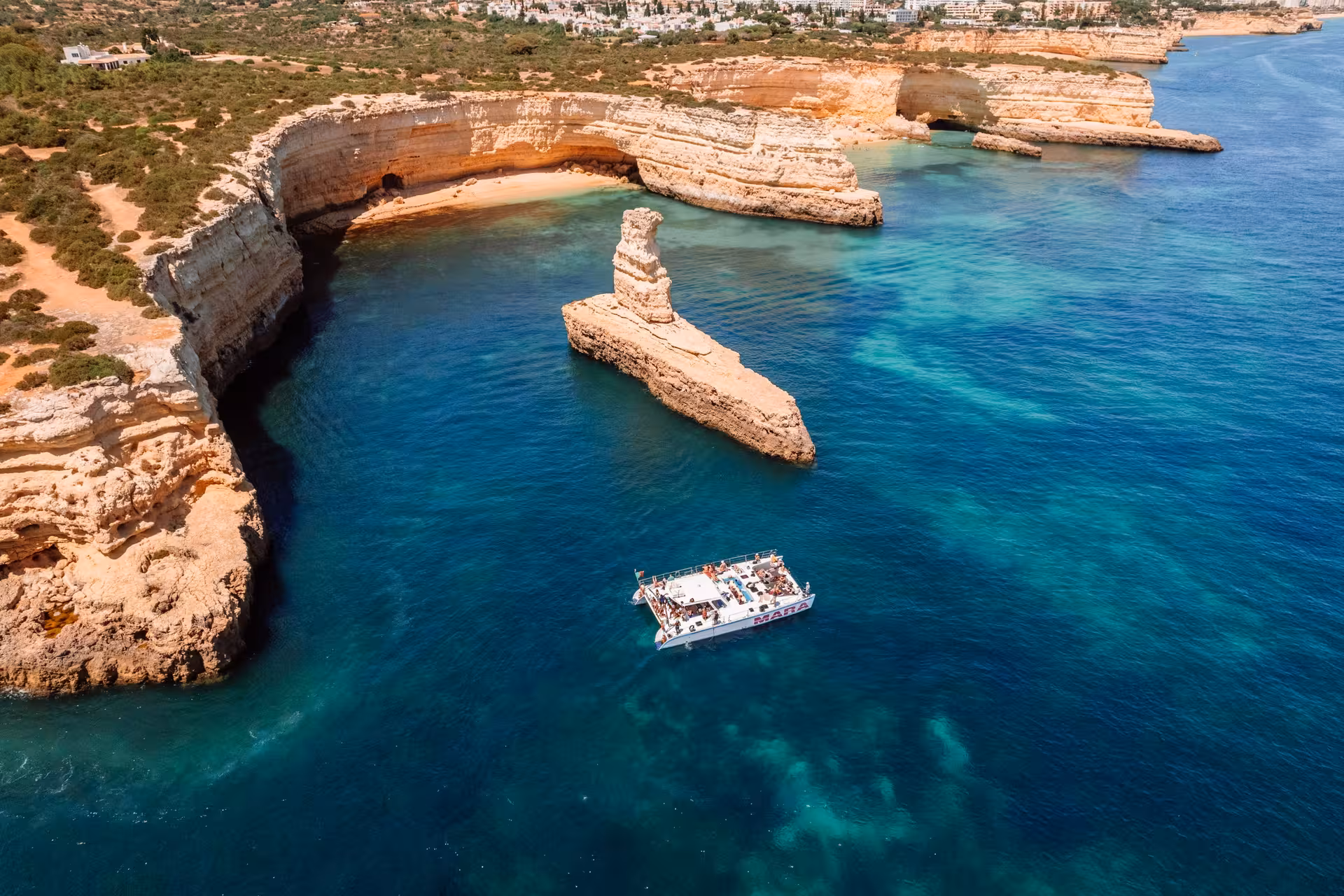 Explore Algarve's rugged coastline on Catamaran MARA, surrounded by azure waters and dramatic limestone formations.