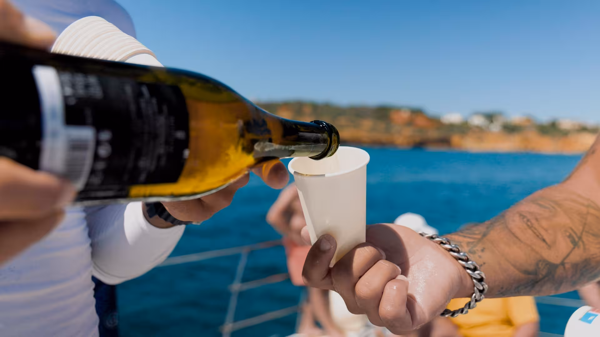 Guests enjoying wine onboard 'Catamaran MARA' with a scenic coastline backdrop, perfect for a relaxing tour.