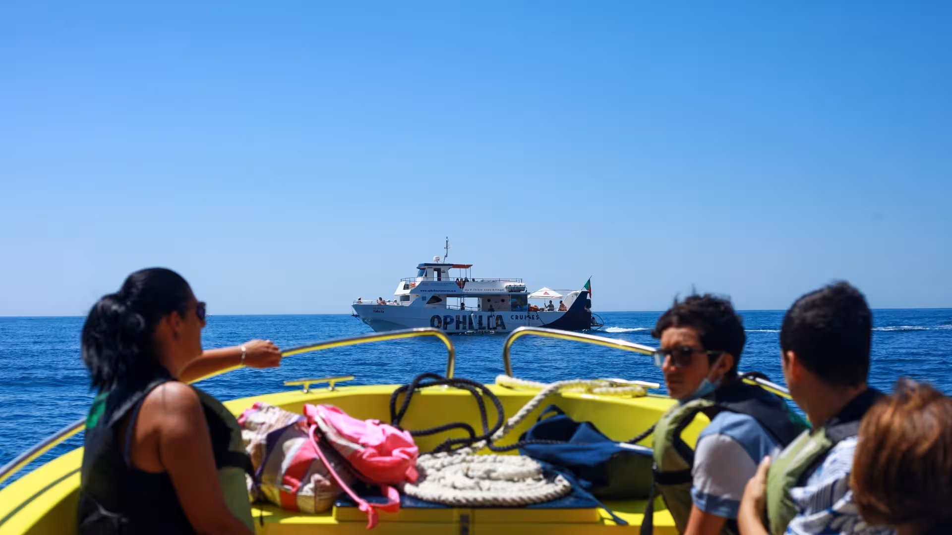 Passengers on a small boat enjoying views of the Catamaran Ophelia cruising the Algarve coastline.