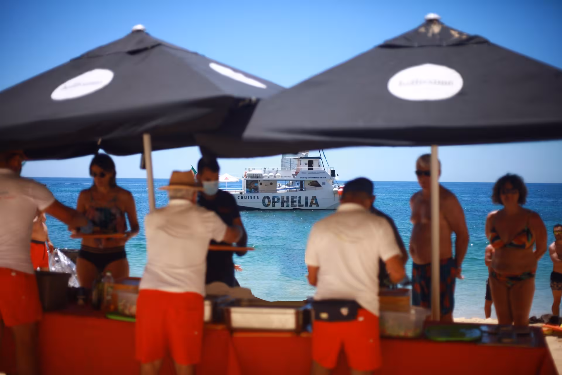 Tourists enjoy a BBQ on the beach with Catamaran Ophelia in the background during the Benagil Caves tour.