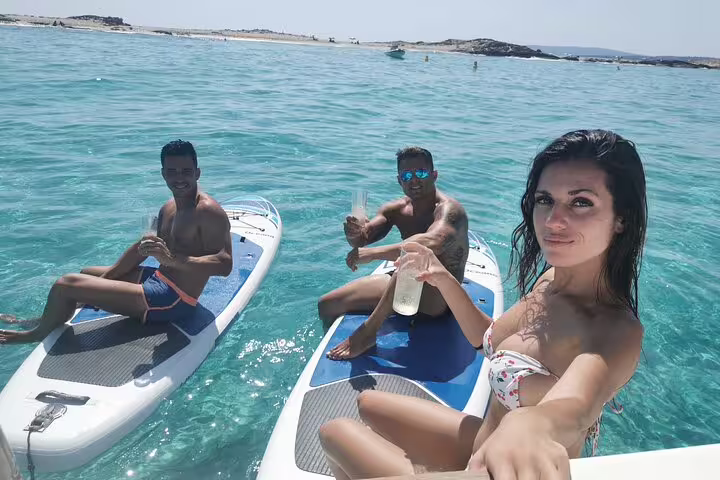 People enjoying paddleboarding and drinks on a catamaran tour in the crystal-clear waters of Formentera and Ibiza.