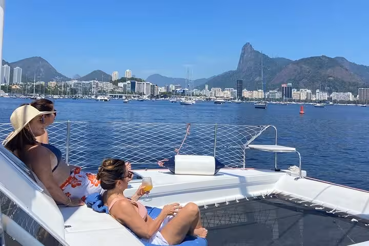 Guests lounging on catamaran net with drinks, private Velas do Rio sail tour with Sugarloaf views