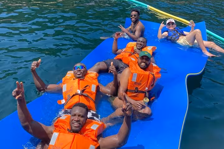 Guests relax on floating mat with life vests and drinks during Velas do Rio catamaran tour open bar