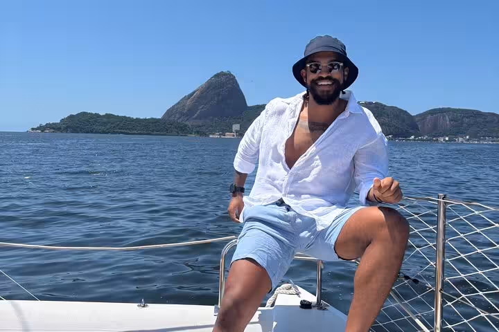 Man posing on catamaran with Sugarloaf Mountain view during Velas do Rio private sailboat tour with BBQ