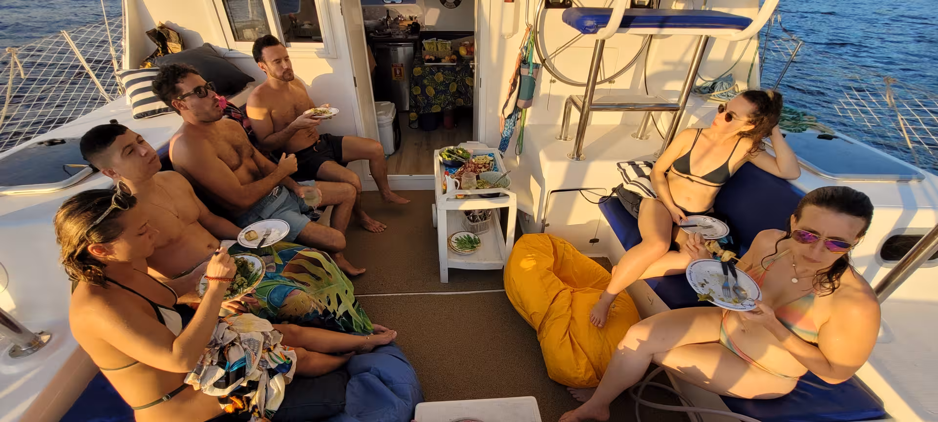 Friends enjoying snacks and sunset vibes aboard Velas do Rio shared catamaran, 3-hour Rio sailing tour