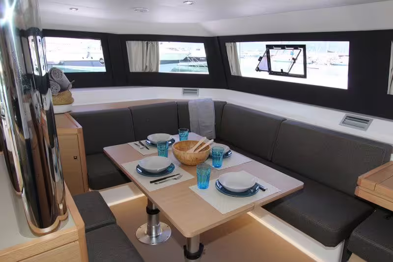 Bright catamaran salon with panoramic windows and set dining table ready for guests on a Gulf of Naples sailing tour