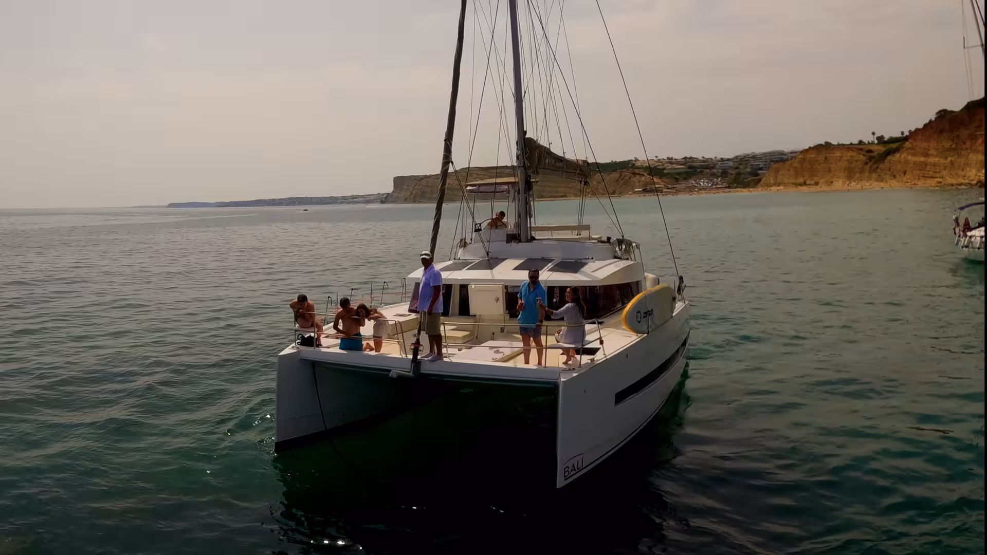 Guests relaxing on Bali catamaran near Lagos Algarve coastline, scenic sunset cruise on Atlantic with cliff views