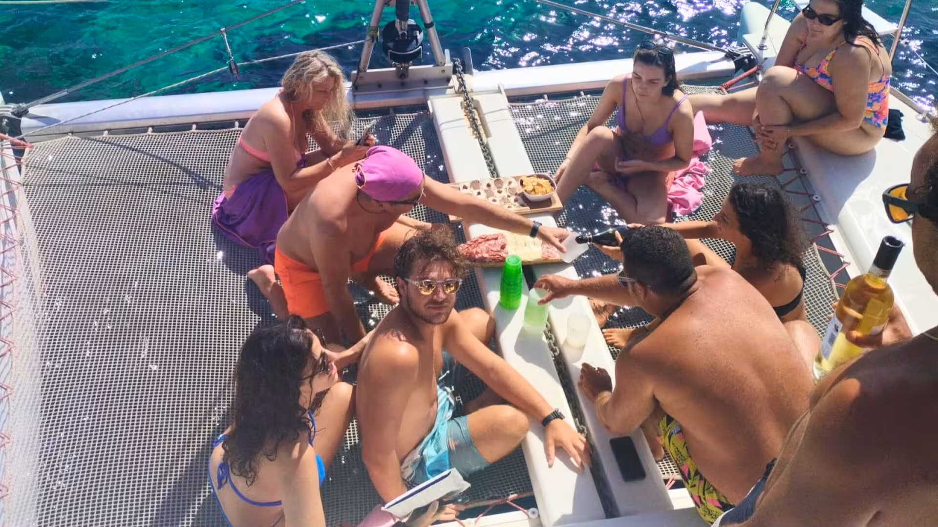 Tourists sharing snacks and drinks on a catamaran deck amid the vibrant blue seas of La Maddalena Archipelago.