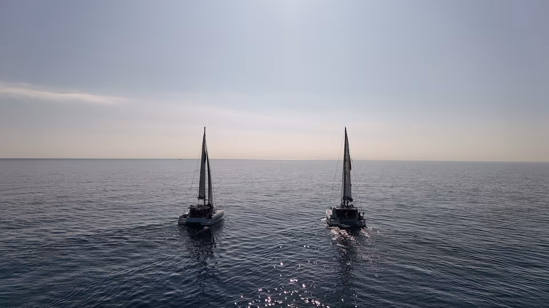 Two catamarans sailing on calm Mediterranean at sunset, Barcelona sea breeze wellness cruise with ocean views